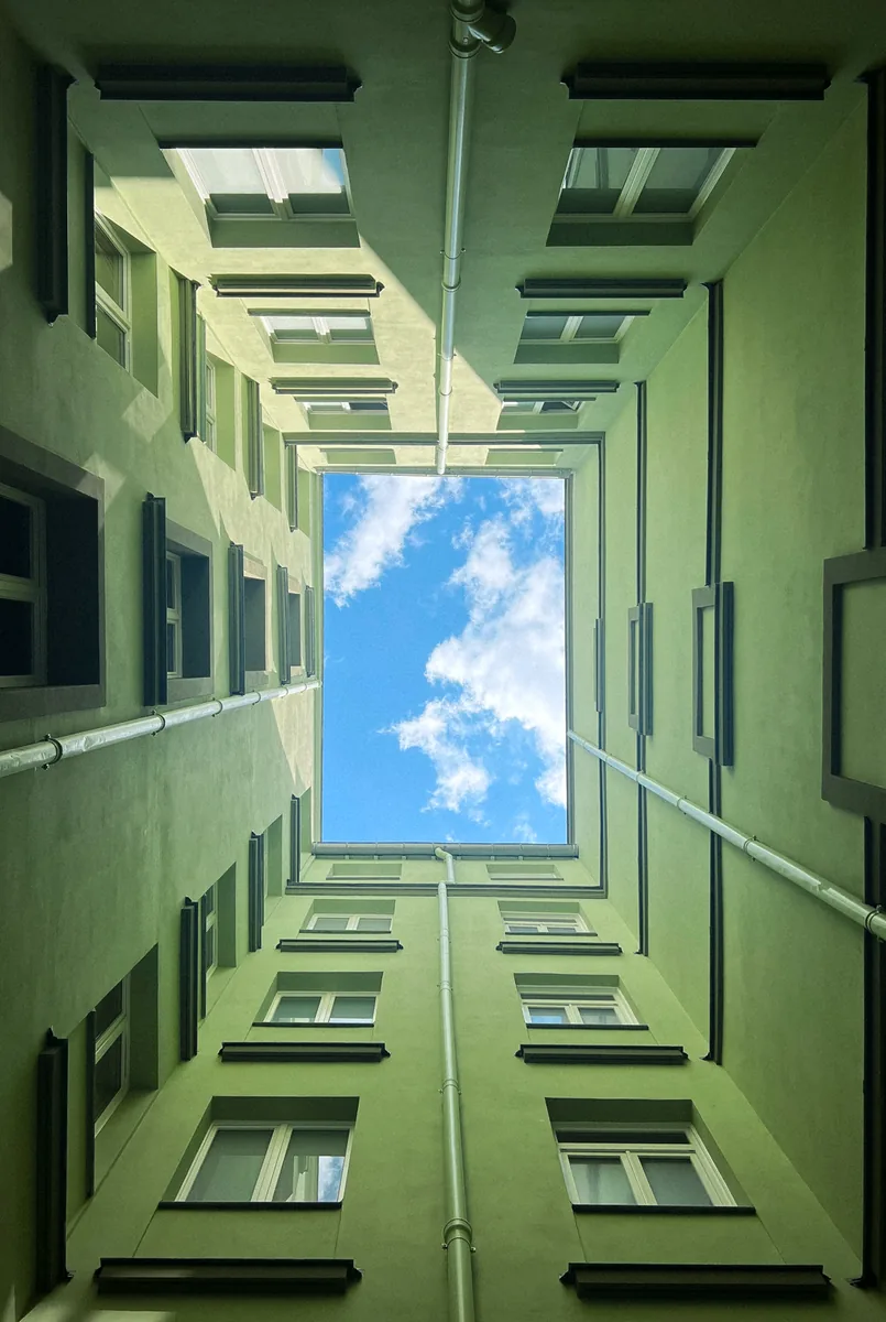 Looking straight up a narrow green courtyard to a rectangle of blue sky.