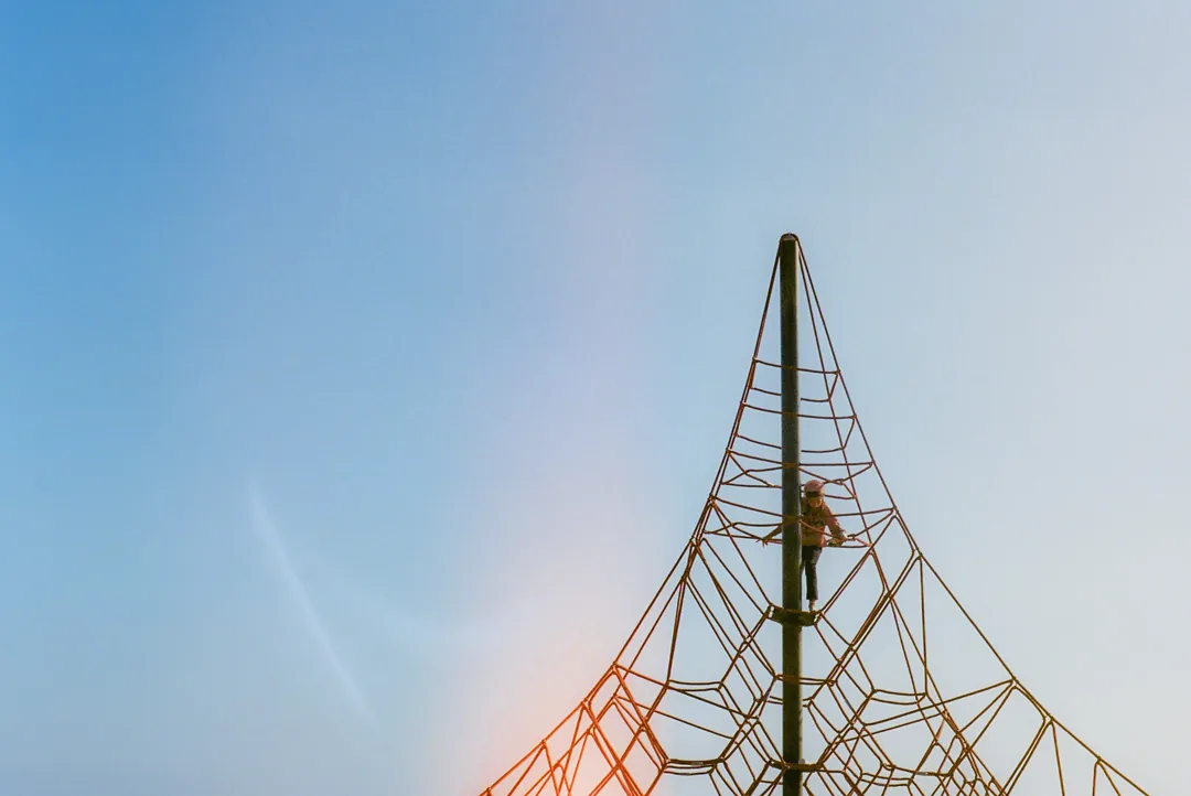 A slender mast strung with a web of orange rigging against a pale sky.