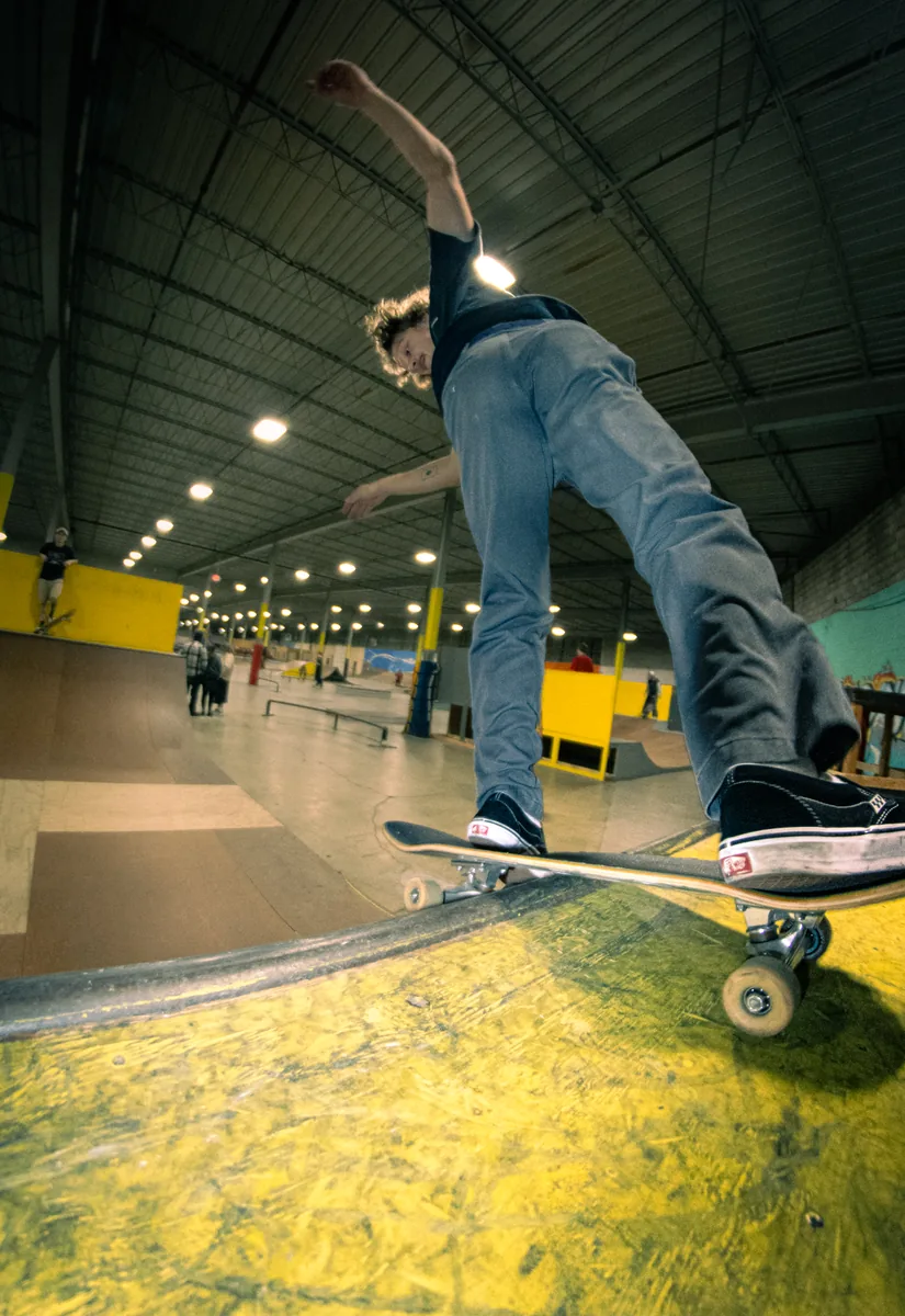 A skater riding the yellow lip of a bowl, arm thrown up for balance.