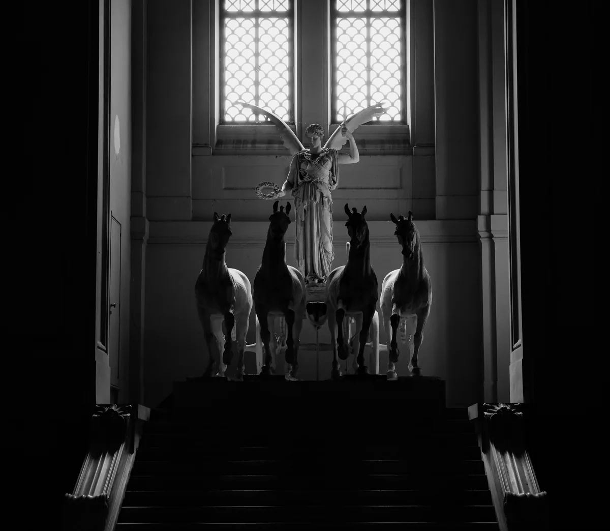 Four horse statues abreast on a dark museum stair beneath a winged figure.
