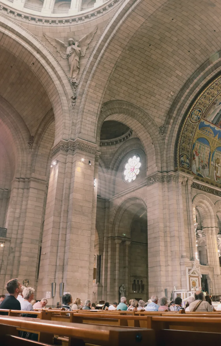 Stone arches and a rose window above the pews inside Sacré-Cœur, Paris.