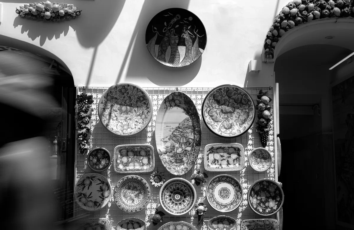 A wall of patterned ceramic plates in black and white, a figure blurred past it.