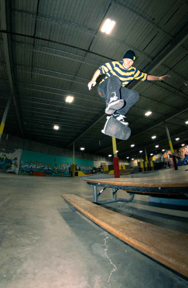 A skater airborne over a wooden ramp in an indoor park.