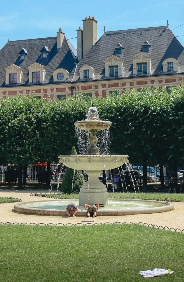 A child leaning over the basin of the Place des Vosges fountain, Paris.