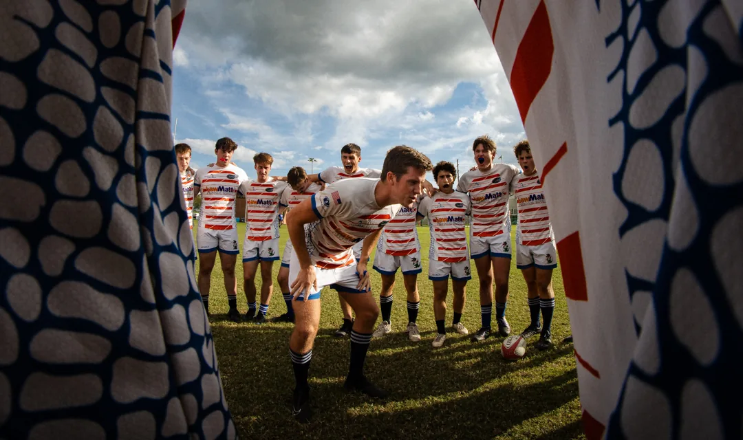 A rugby side lined up on the grass, framed between two flags in the foreground.