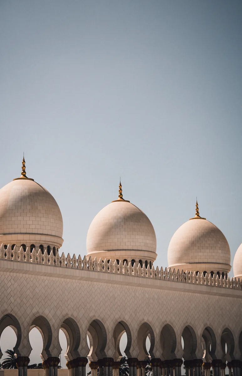 Three domes of the Sheikh Zayed Grand Mosque above an arcaded parapet.