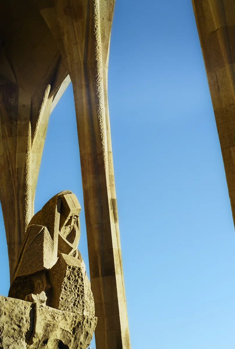 Looking up a slot of blue sky between tall pale columns, a carved figure at their foot.