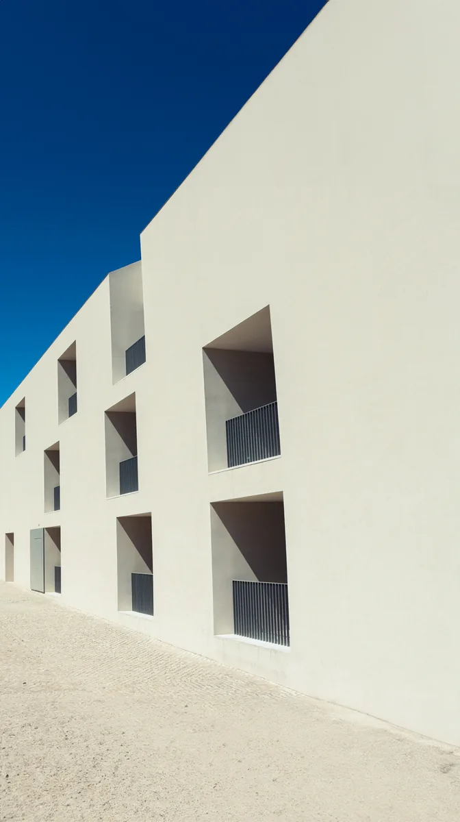 Recessed windows in a white concrete facade under raking sun and deep blue sky.