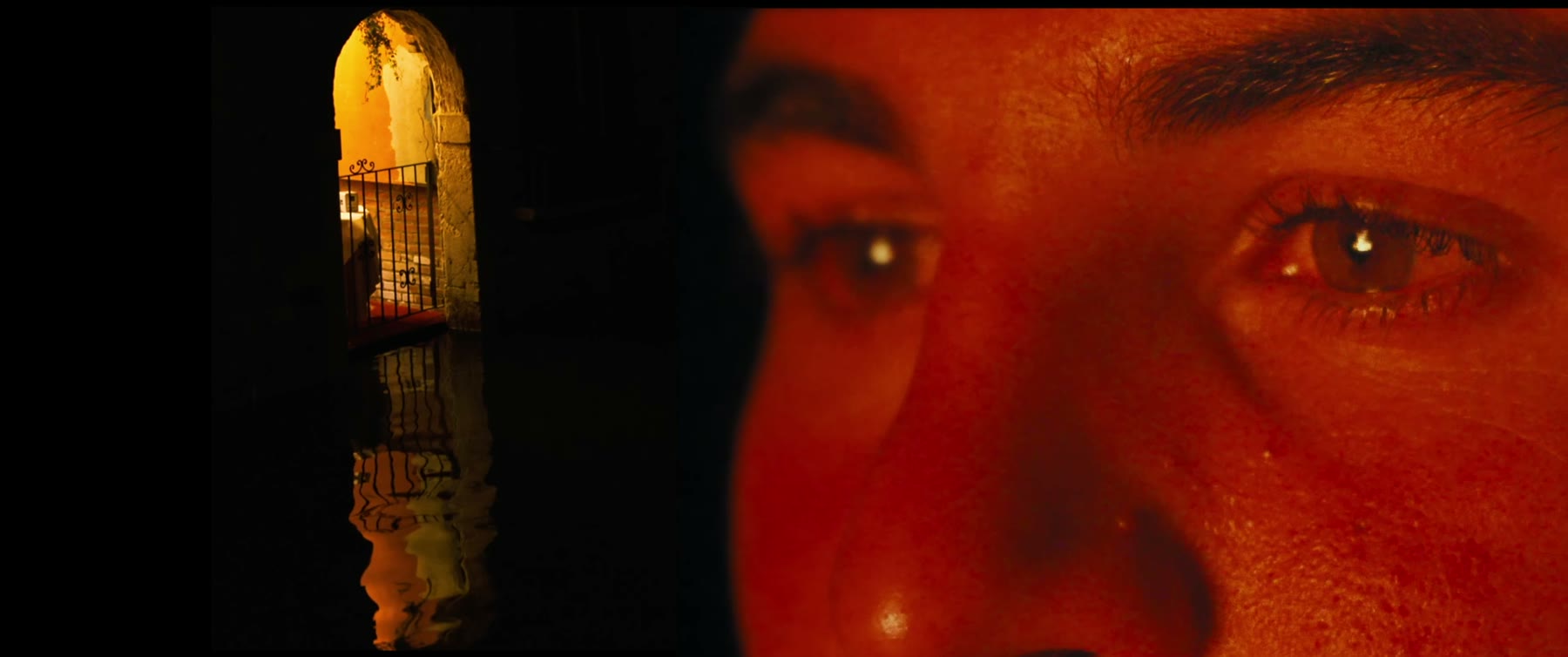 Still from Paixão Calejada: a face lit deep red beside a lit archway.